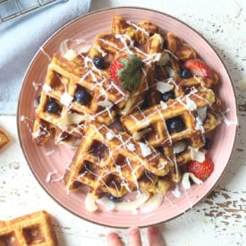 Waffles served on a pink plate topped with berries.