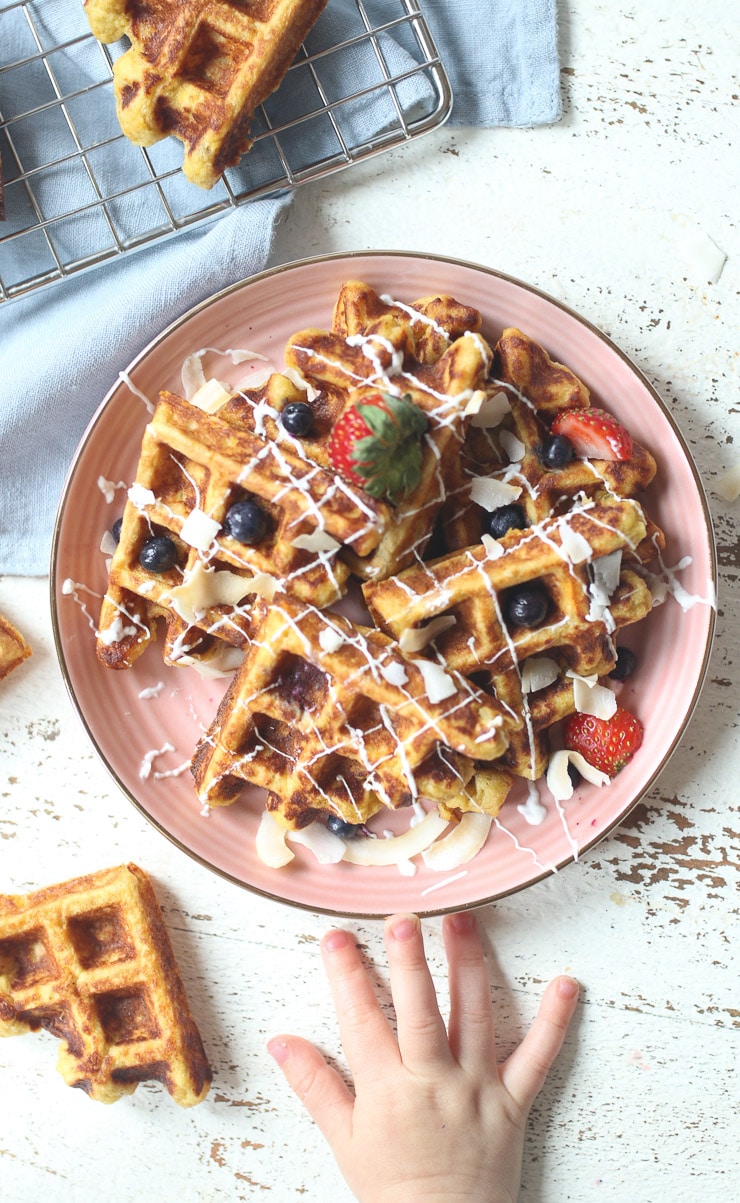 Waffles served on a pink plate topped with berries. 