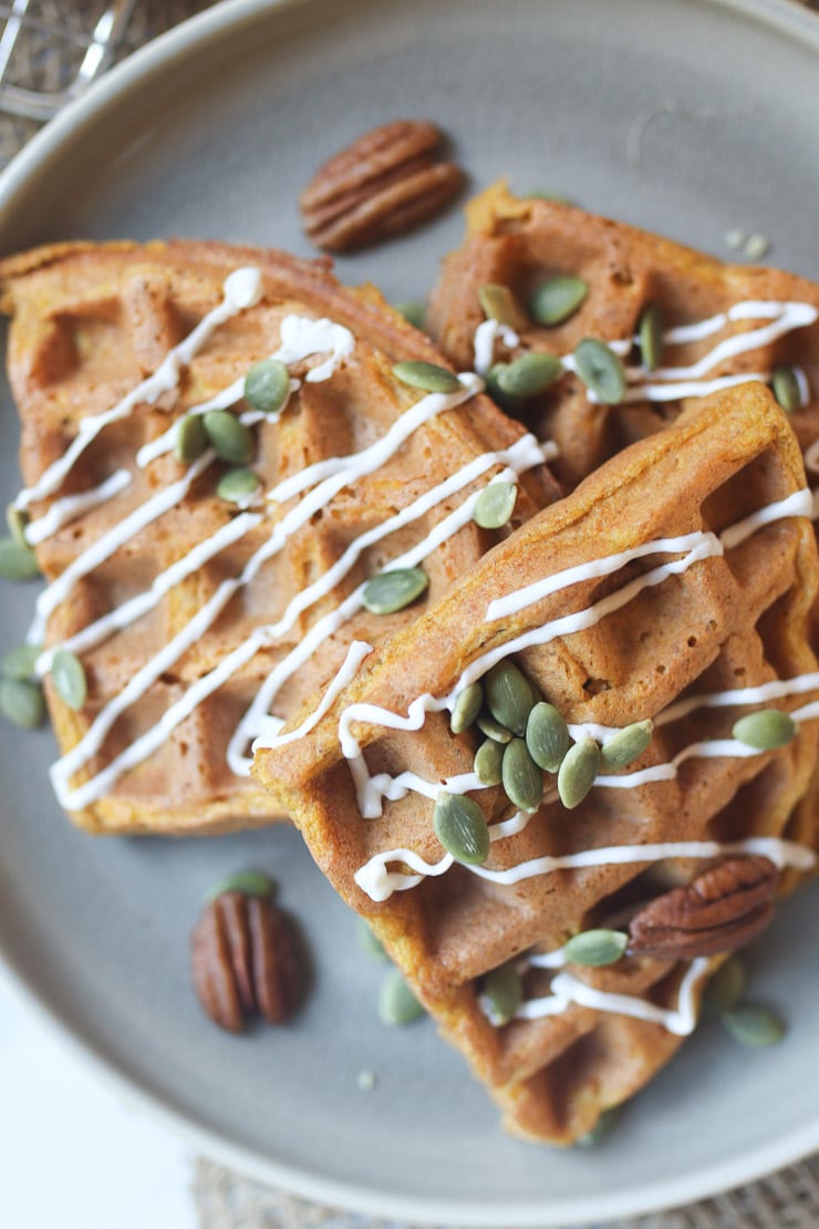 Waffles on a grey plate topped with pumpkin seeds and pecans.