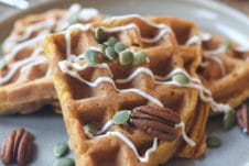 Waffles on a grey plate topped with pumpkin seeds and pecans.