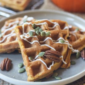 Waffles on a grey plate topped with pumpkin seeds and pecans.
