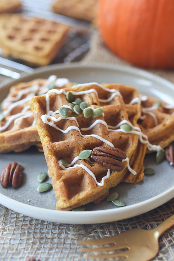Waffles on a grey plate topped with pumpkin seeds and pecans.