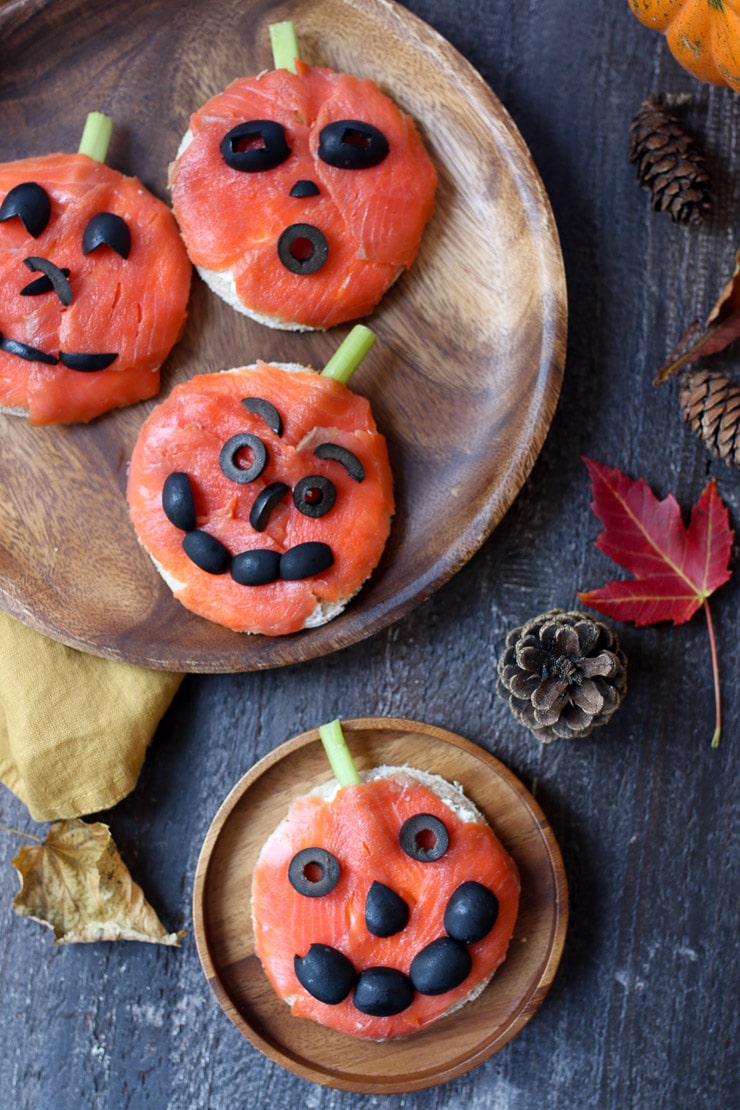 Several smoked salmon pumpkin sandwiches on brown serving plates, as Halloween sandwich ideas.