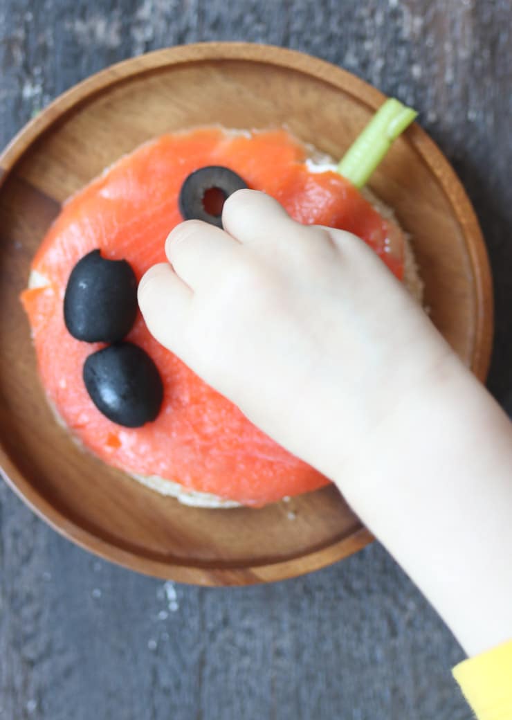 Toddler hand reaching for olive on halloween smoked salmon sandwich. 