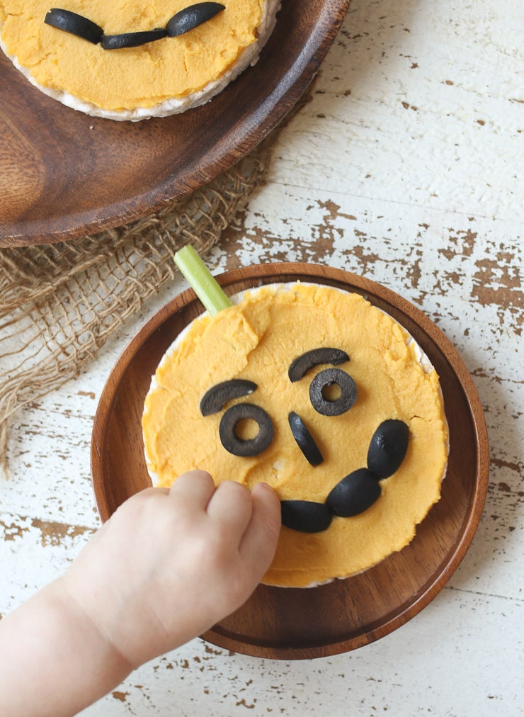 Toddler reaching for rice cakes topped with pumpkin hummus.