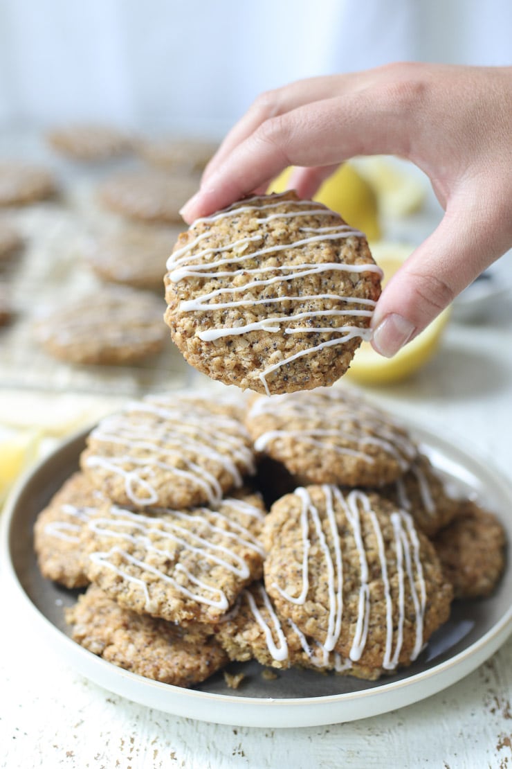 Hand holding lactation cookie above a plate of cookies drizzled with a glaze.