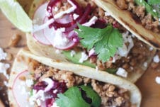 Three tacos on a wooden plate.