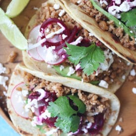 Three tacos on a wooden plate.