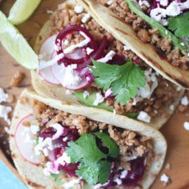 Three tacos on a wooden plate.