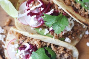 Three tacos on a wooden plate.