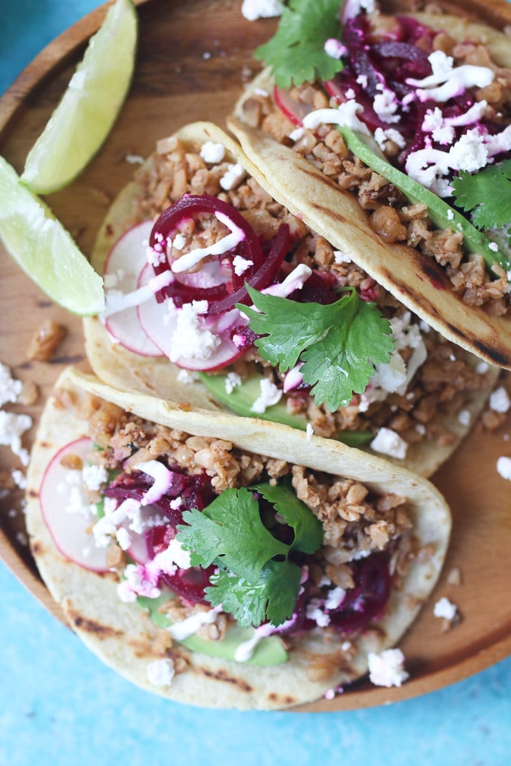 Three cauliflower and walnut tacos on a wooden plate.