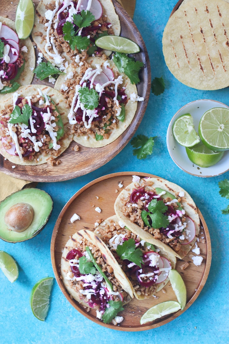 Birds eye view of multiple tacos on two wooden plates garnished with cilantro and pickled beets.