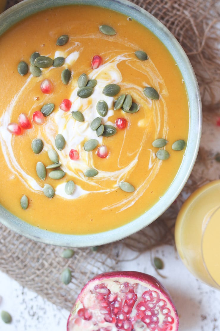 birds eye view of Orange soup in a bowl topped with pomegranates and pumpkin seeds. 