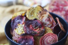 Crispy colourful beet chips in a black bowl.