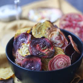 Crispy colourful beet chips in a black bowl.