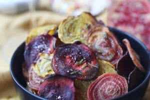 Crispy colourful beet chips in a black bowl.