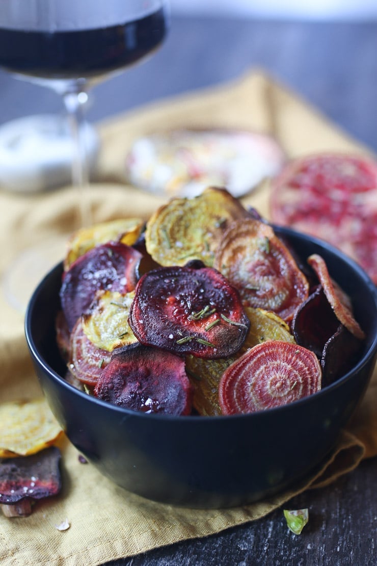 Crispy colourful beet chips in a black bowl.