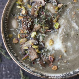 Bowl of mushroom soup topped with nuts and herbs.