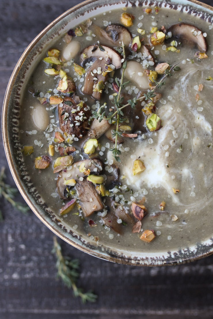 Bowl of mushroom soup topped with nuts and herbs. 