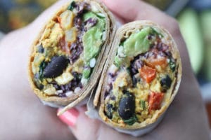 Hands holding two halves of breakfast burrito.