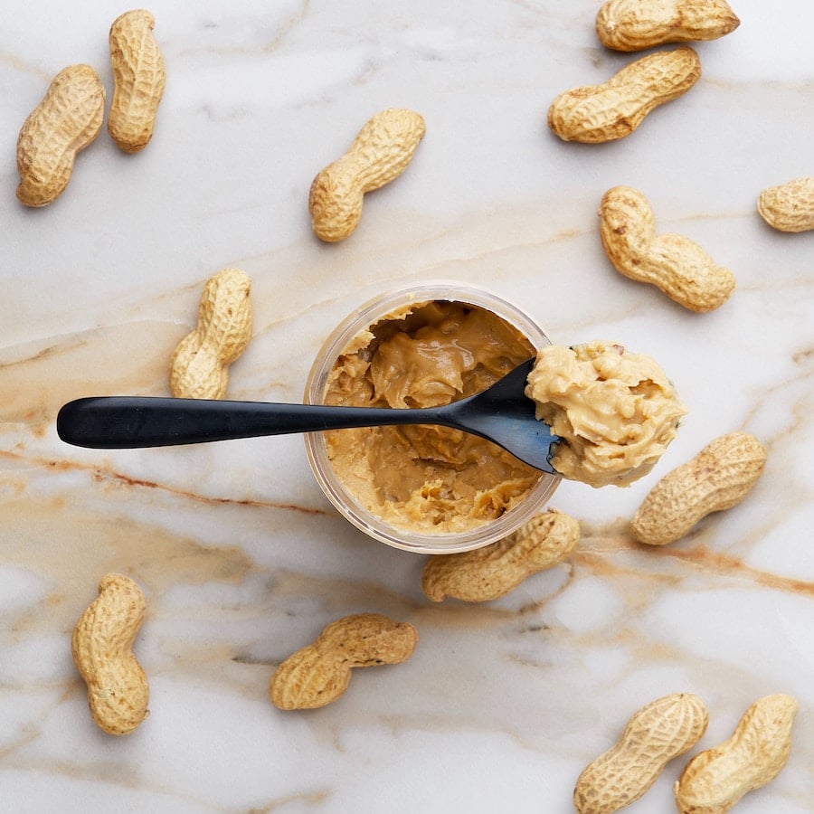 Spoon of peanut butter next to peanuts