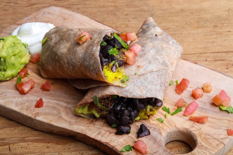 Two burritos served on a wooden cutting board.