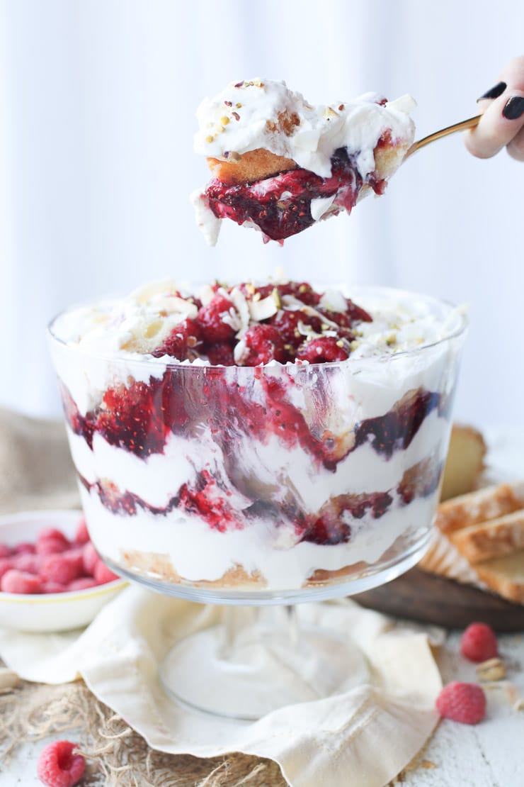 Hand scooping out serving of trifle from a clear glass dish. 