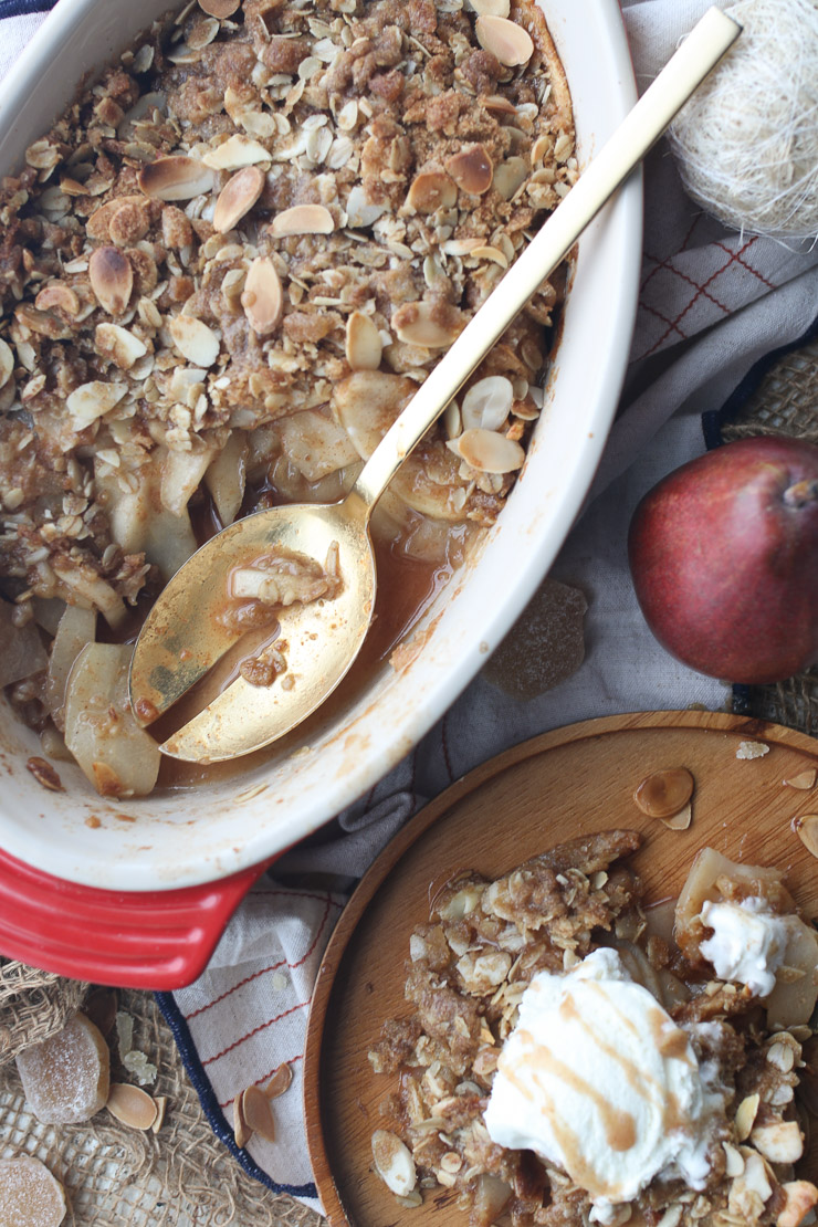 Pear and ginger crisp in a casserole dish next to a plate with a serving of crisp. 