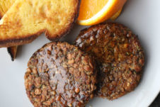 Two vegan breakfast sausage patties next to orange slices and toast on a plate.