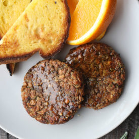 Two vegan breakfast sausage patties next to orange slices and toast on a plate.