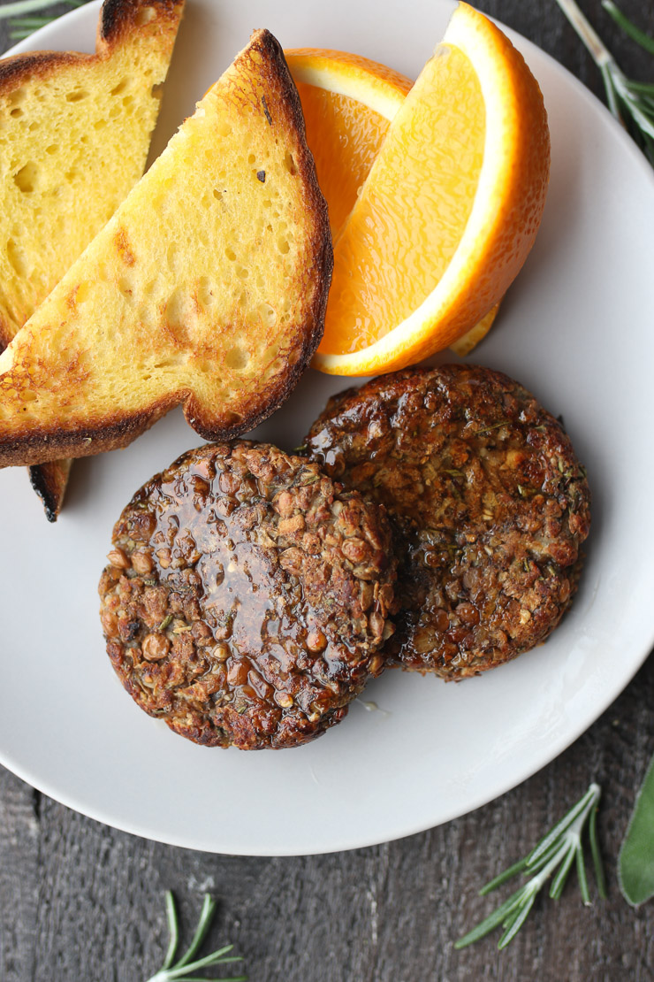 Two vegan breakfast sausage patties next to orange slices and toast on a plate.