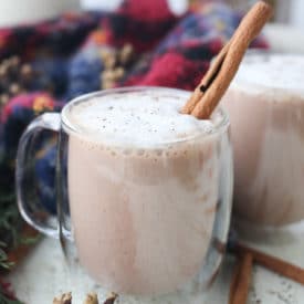 Egg nog in a glass mug topped with a cinnamon stick.