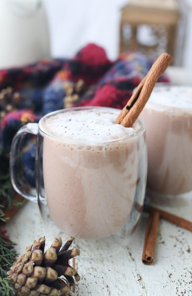 Egg nog in a glass mug topped with a cinnamon stick.