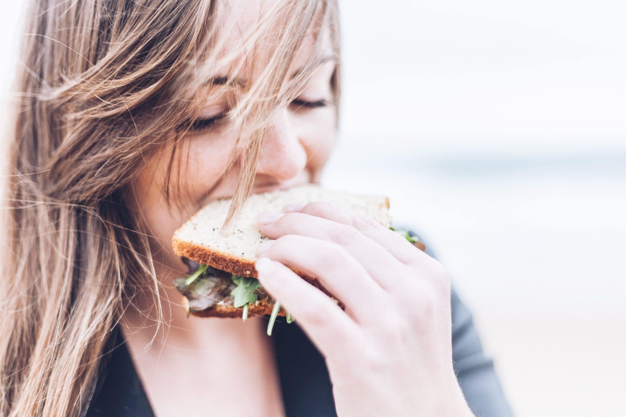 Woman with PCOS taking a bite out of sandwich. 