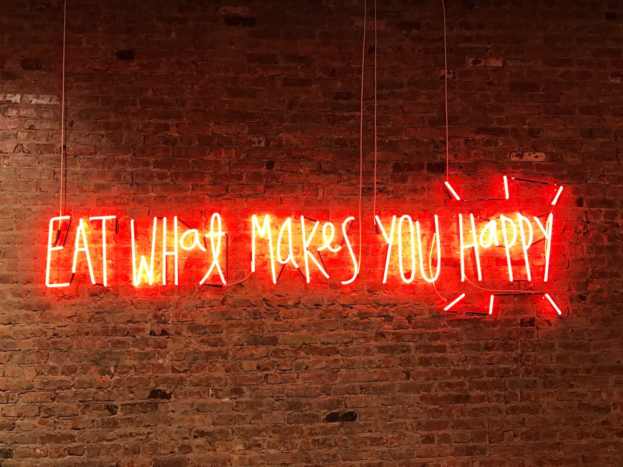 "eat what makes you happy" in lights written on a brick wall 