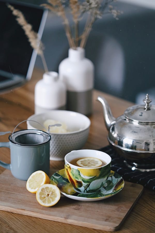 Mug of tea with lemon next to teapot. 