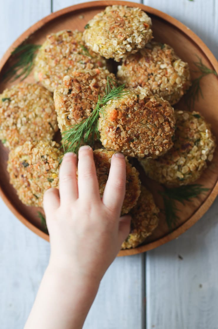 Toddler reaching for a fish cake on a wooden plate.