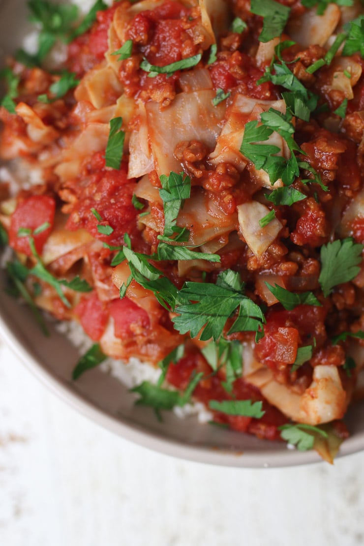 Close up of unstuffed cabbage roll dish in a bowl topped with parsley.