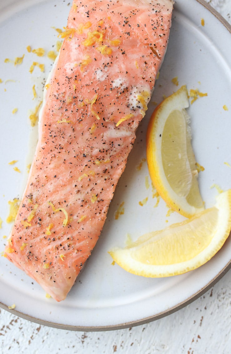 Pink salmon on a white plate garnished with lemon zest.