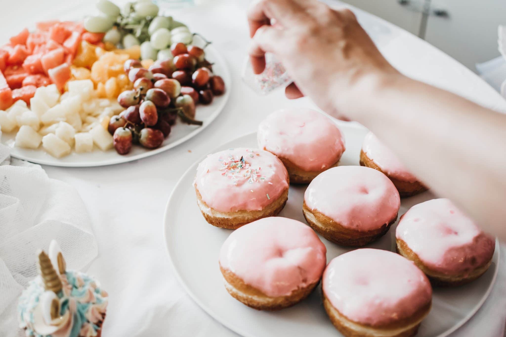 person putting sprinkles on donut with a fruit plate in the background 