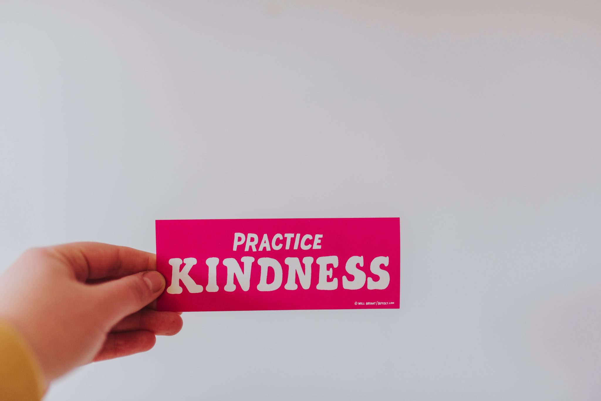 person holding pin sign that says "practice kindness" as a way to challenge food police