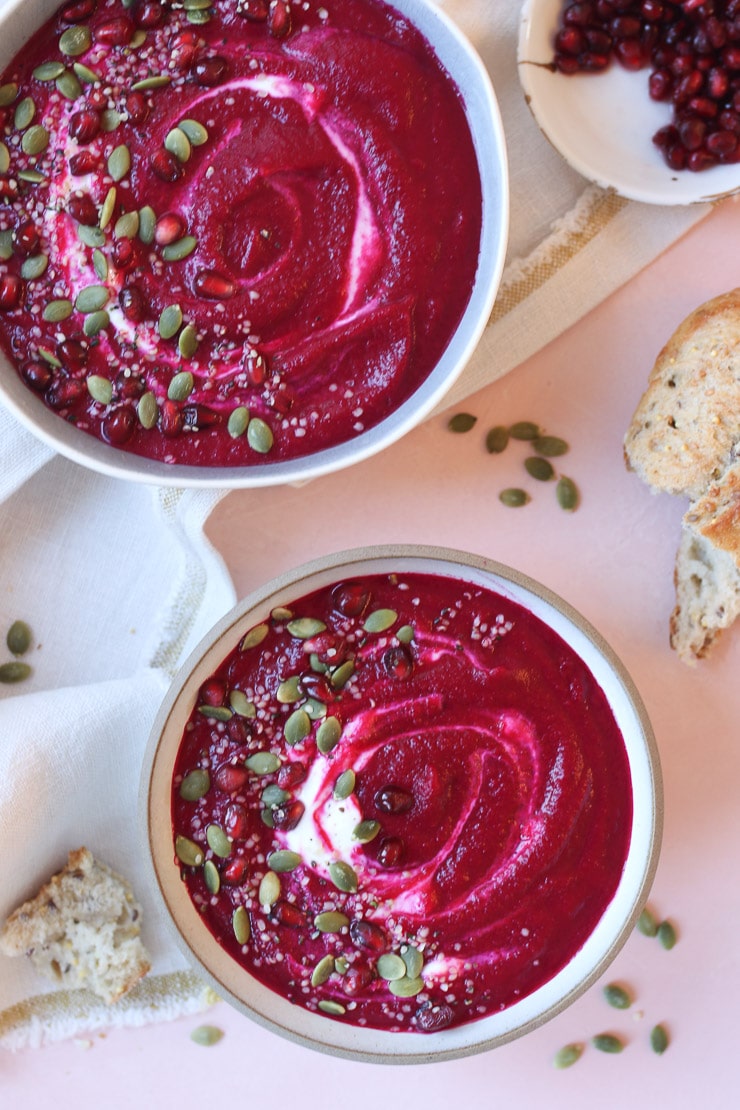 two red beet soup in a bowl topped with pomegranate seed and pumpkin seeds