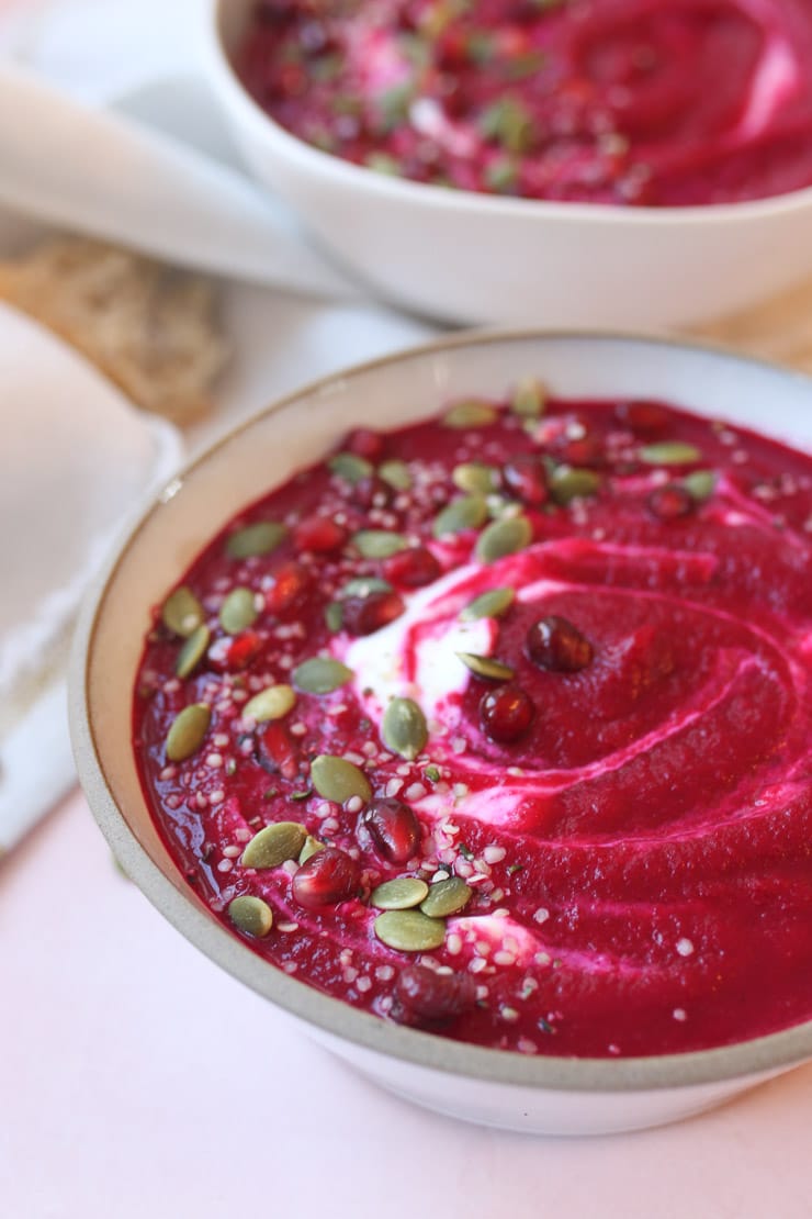 red beet soup in a bowl topped with pomegranate and pumpkin seeds 