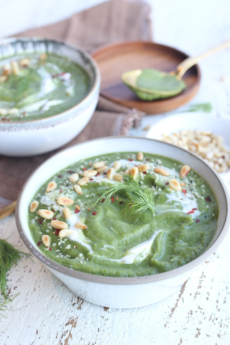 Vegan broccoli soup in a bowl garnished with pine nuts and dill .