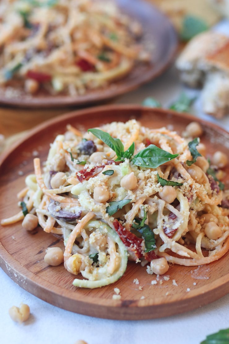 Hummus pasta sauce and zucchini noodles topped with a basil leaf on a wooden plate.