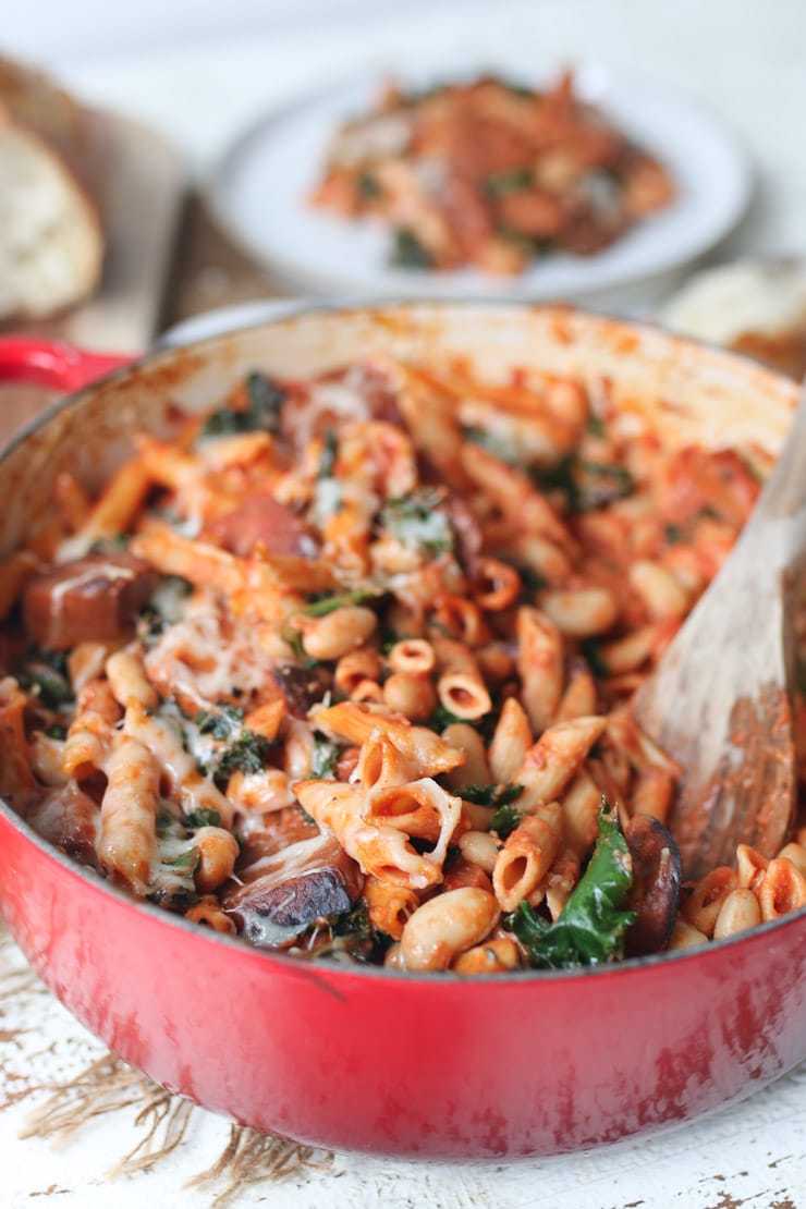 Pasta bake in red casserole dish with wooden spoon in the middle