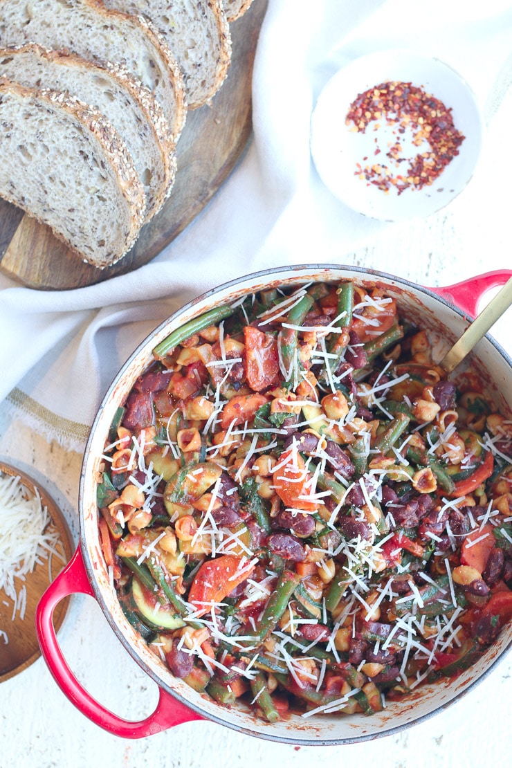 birds eye view of vegan minestrone skillet pasta in a red pot with bread and chili flakes in the background