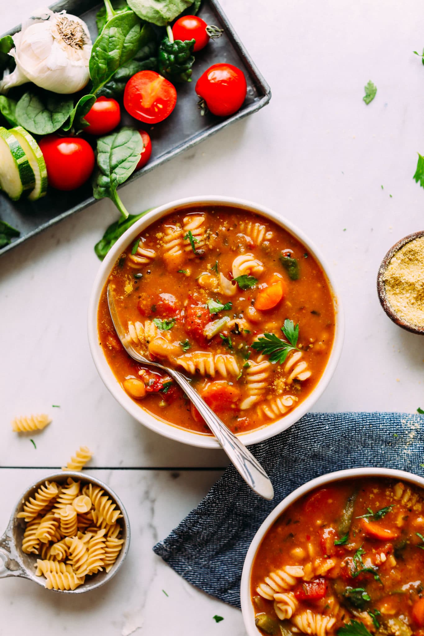 A bowl filled with vegan minestrone soup with a spoon inside on a light pink background.