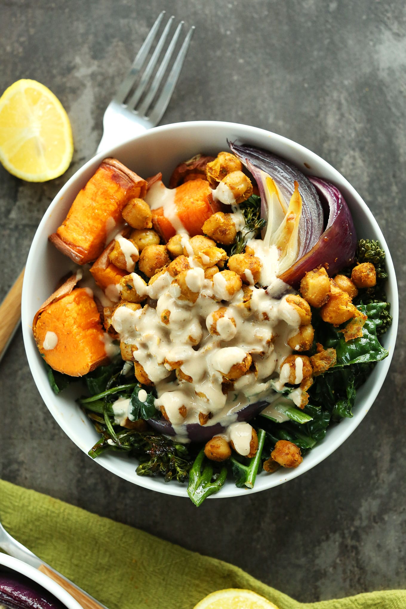 birds eye view of sweet potato chickpea buddha bowl garnished with tahini served with a silver fork and a fresh lemon wedge