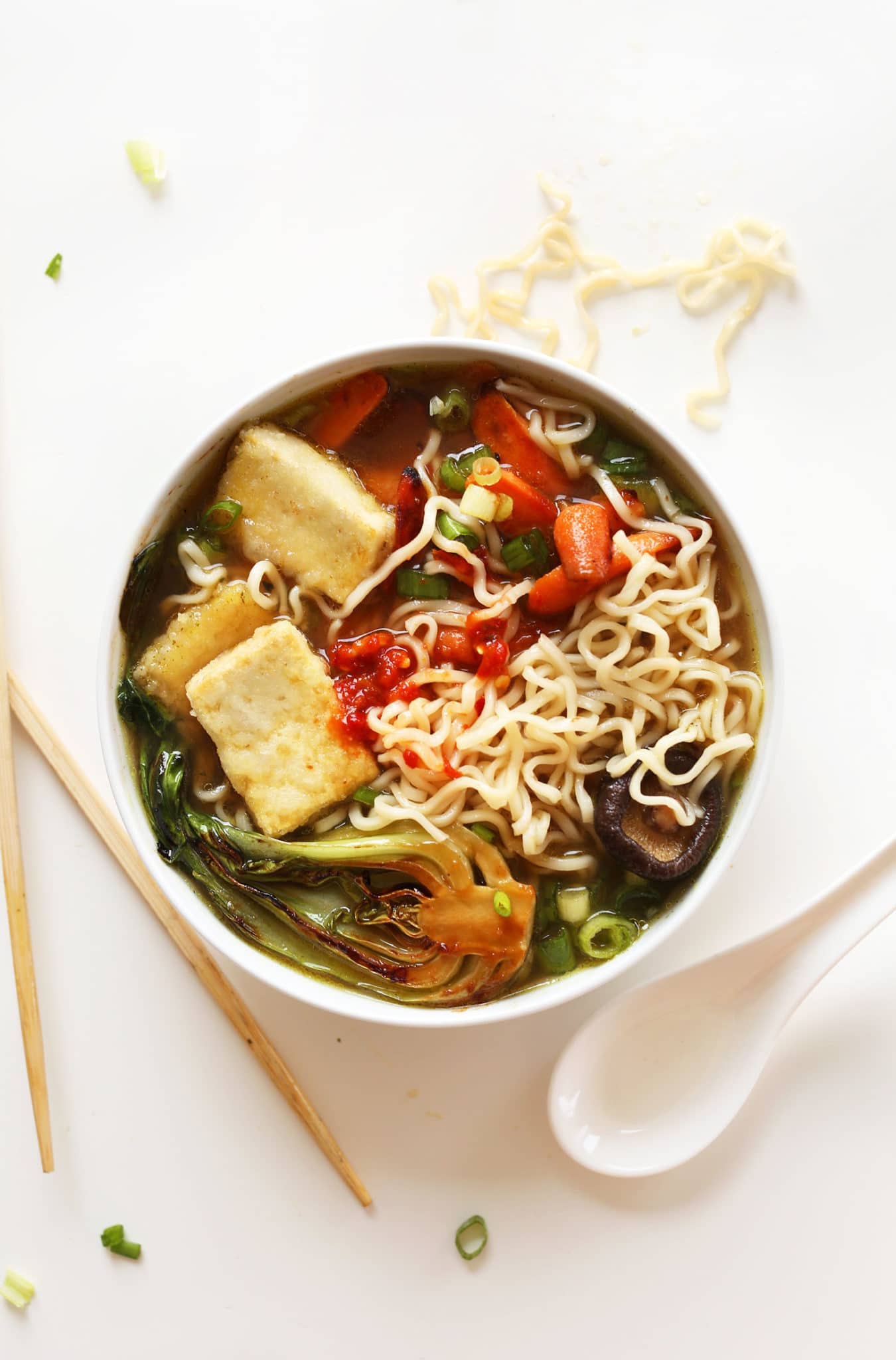 A bowl vegan ramen with tofu, bok choy, and green onions on top on a white background.